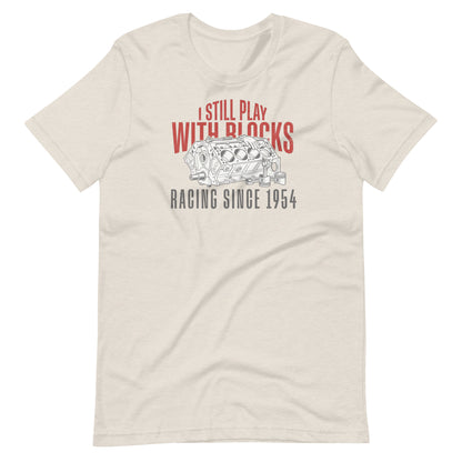 I Still Play With Blocks Tee, Heather Dust front view — bare V8 block line art with slogan print, Marque automotive apparel