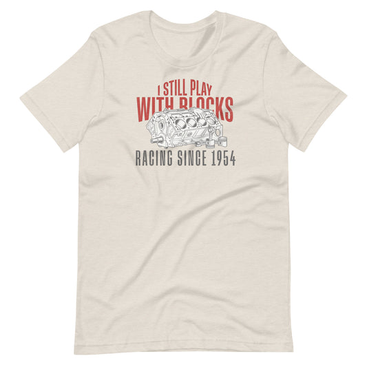 I Still Play With Blocks Tee, Heather Dust front view — bare V8 block line art with slogan print, Marque automotive apparel
